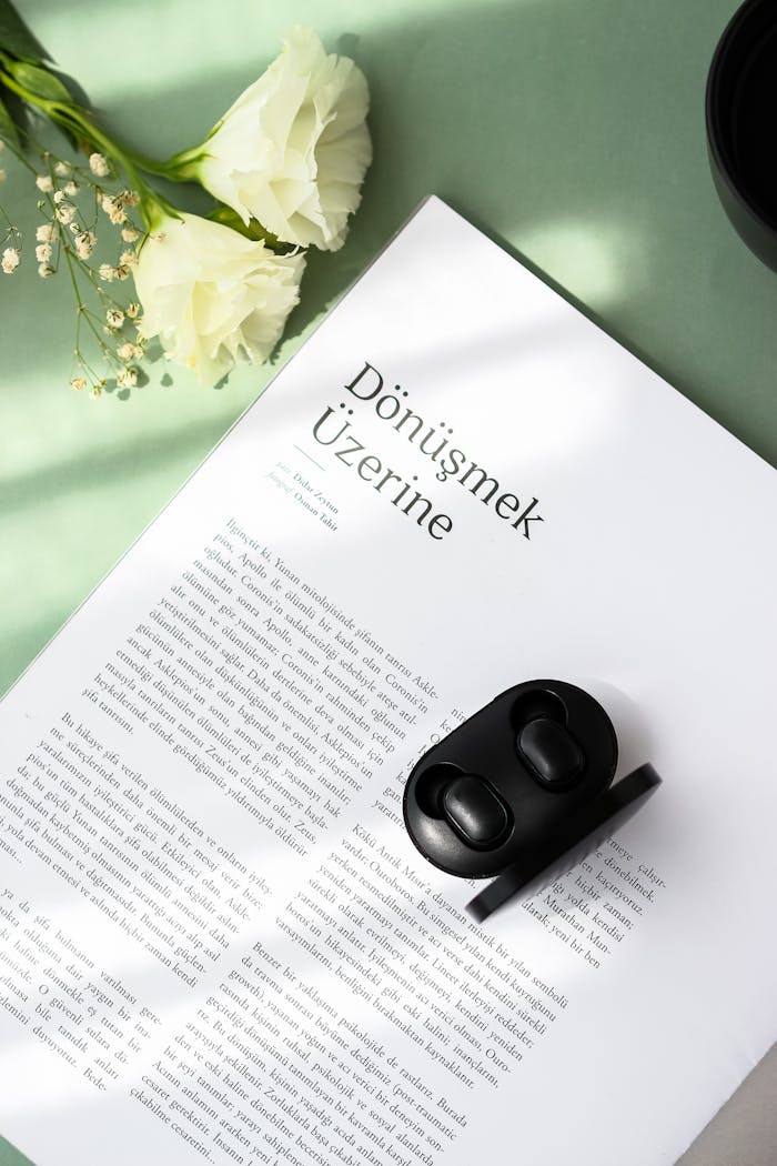 A minimalist composition featuring earbuds on a journal with white flowers, creating a serene still life.