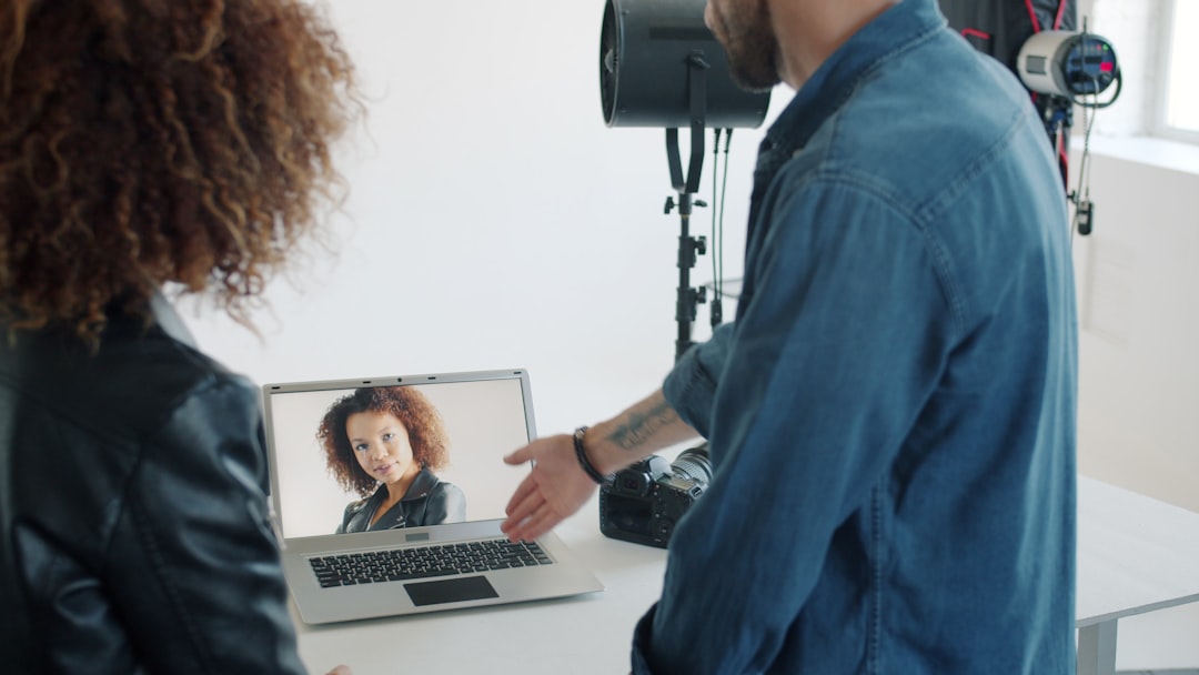Model is watching new photos talking to photographer in studio looking at laptop screen standing indoors in light room. People and communication concept.